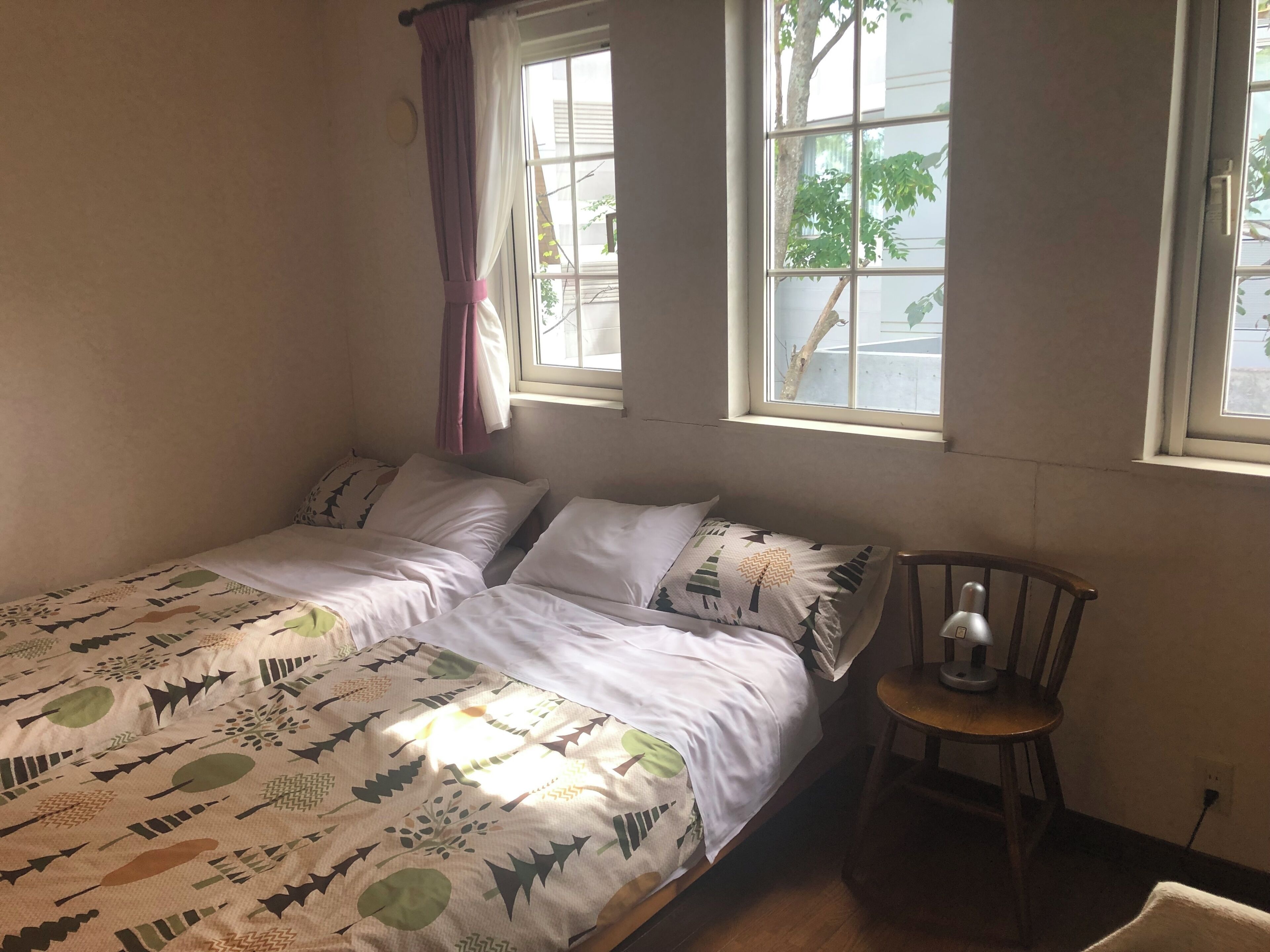 A bedroom with a bed, two windows, a chair, and a lamp.