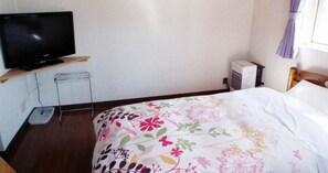 A bedroom with a bed, a television on a shelf, a small table, and an air conditioning unit. - Pension Locomotion (Kutchan)