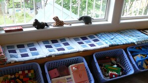 A child's play area with a window view, a quilted mat, and storage bins filled with toys. - Pension Locomotion (Kutchan)