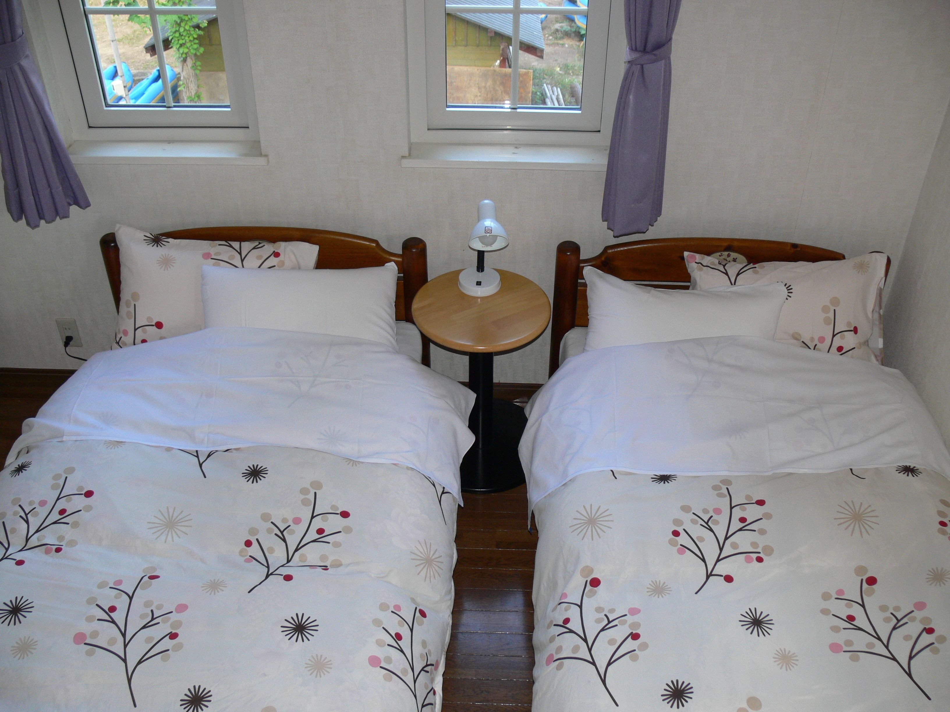 A double bed with floral bedding, a bedside table with a lamp, and a window with curtains.