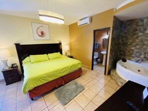 A hotel room with a bed, bedside lamps, a bathroom with a bathtub, and a stone wall. - Hotel Puerto Libre (Puerto Barrios)