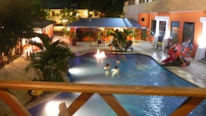 A pool area with a water slide, surrounded by palm trees and a building with multiple balconies. - Hotel Puerto Libre (Puerto Barrios)