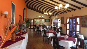 A restaurant with wooden beams and a high ceiling, tables with white tablecloths, and a view through the windows. - Hotel Puerto Libre (Puerto Barrios)