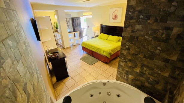 A modern hotel room with a large bathtub, a bright yellow bed, and a stone wall. - Hotel Puerto Libre (Puerto Barrios)