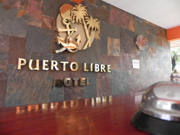 Una recepción con un cartel del Hotel Puerto Libre, que presenta un logo con un ancla y una palmera.