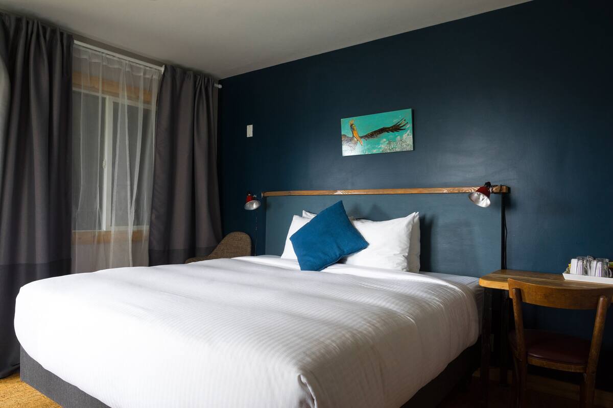 Hotellihuone, jossa on suuri sänky, puinen pääty ja pieni pöytä sekä tuoli.