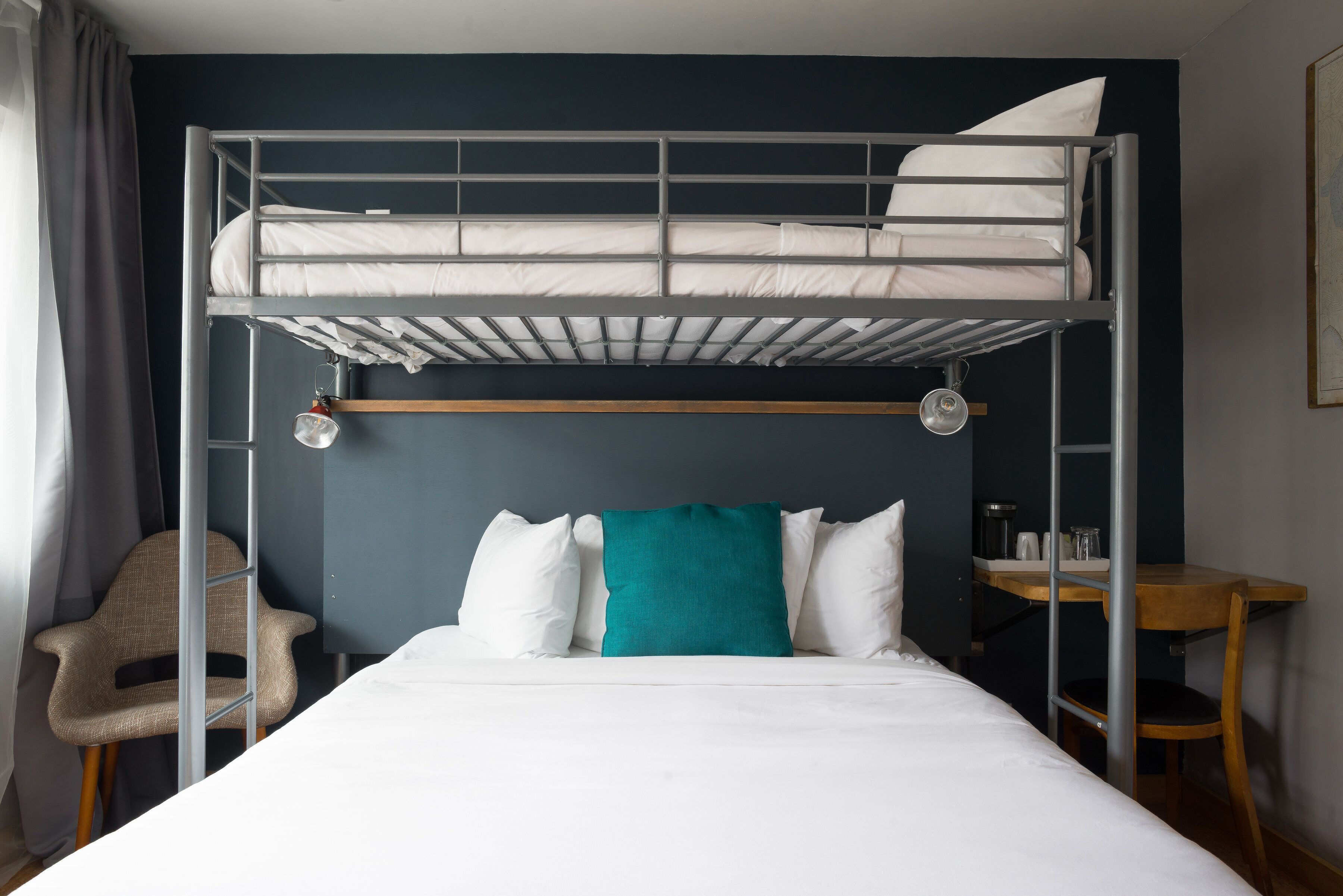 A bunk bed with white bedding, a teal pillow, and a chair.