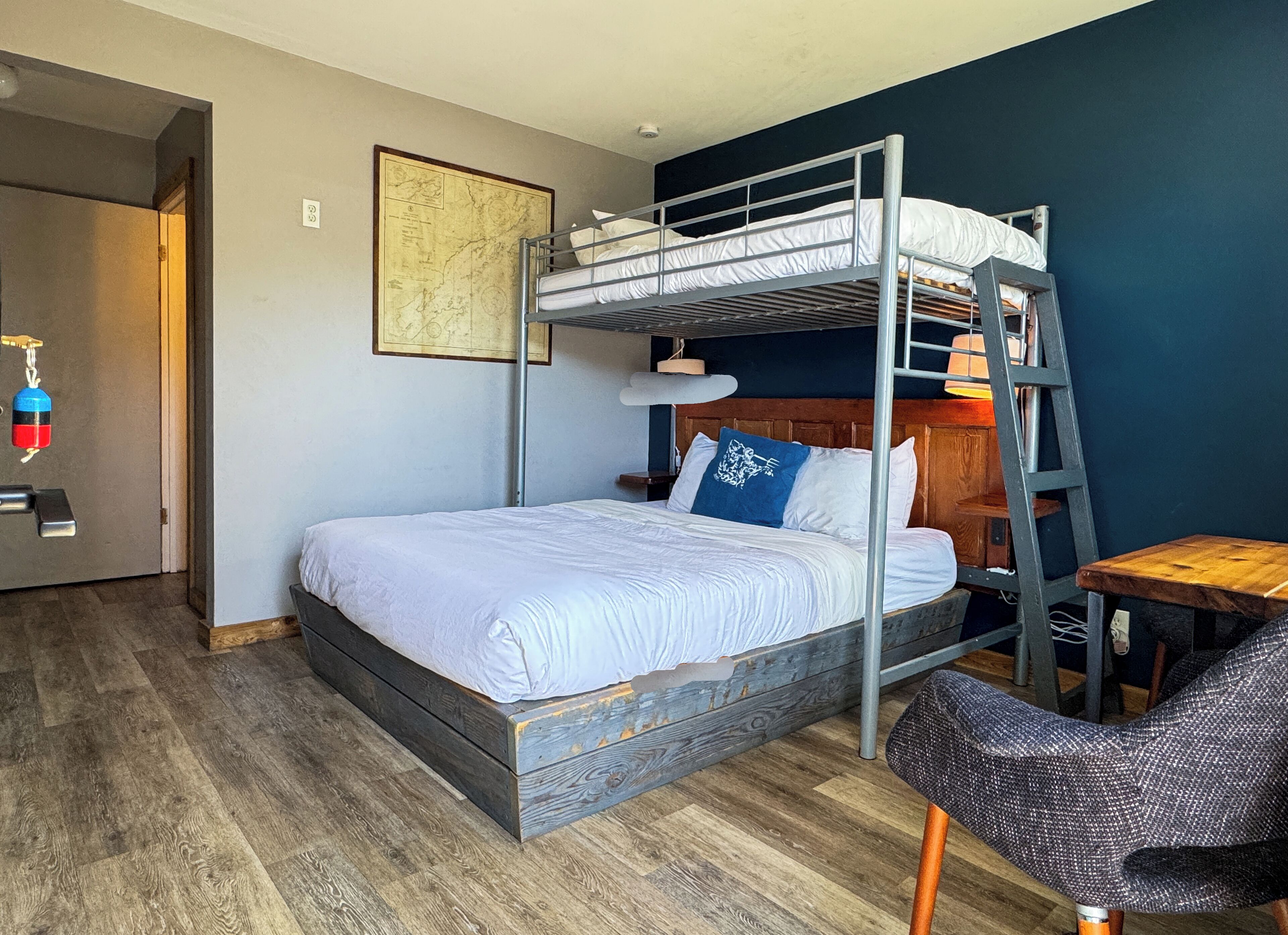 A bunk bed room with a wooden floor, a desk, a chair, and a map on the wall.