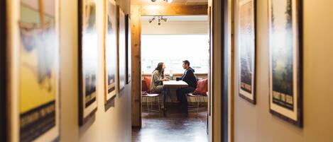 A hallway with framed pictures on the walls, a wooden ceiling, and a window at the end.