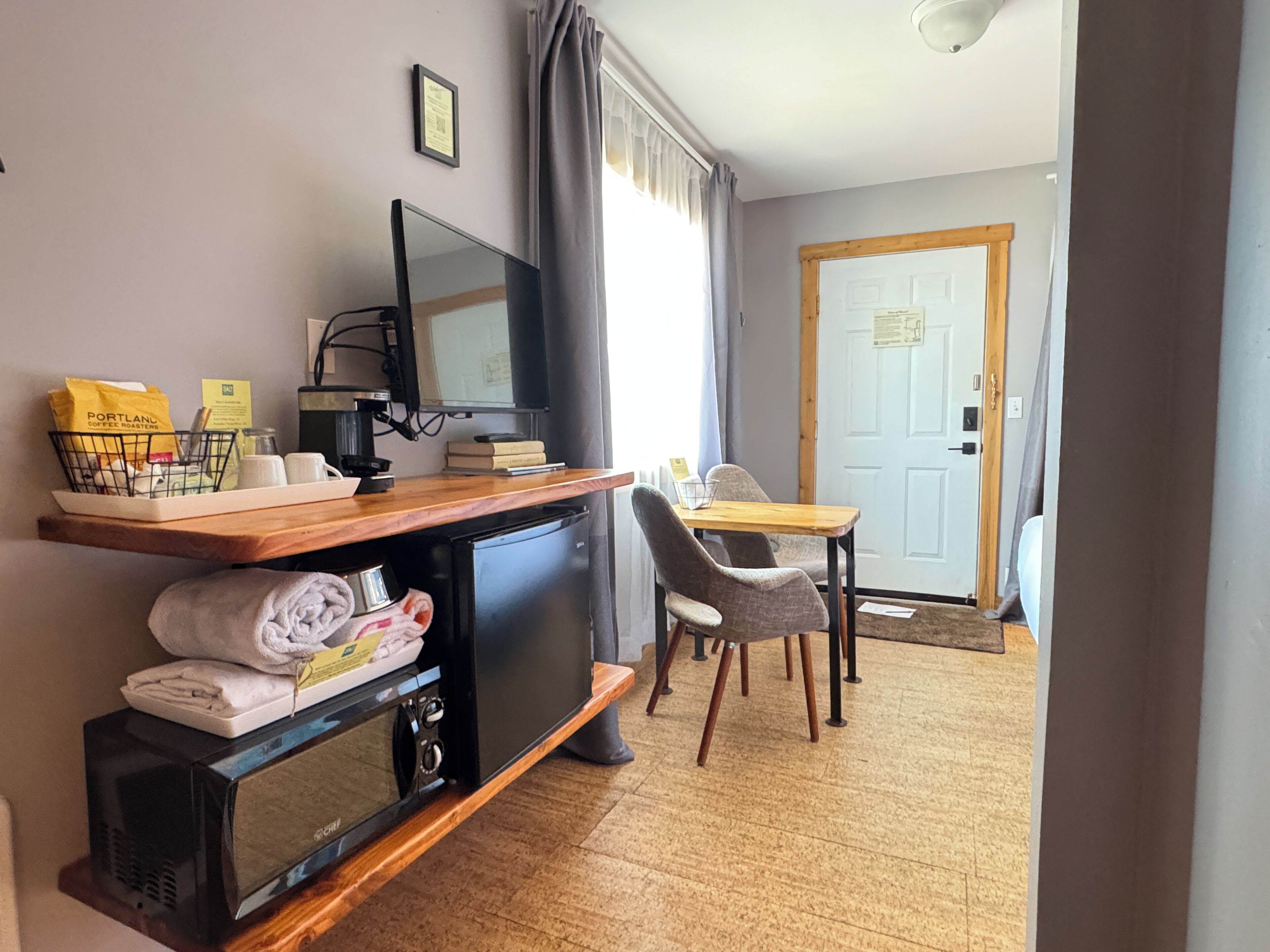 Habitación compacta con kitchenette, televisor, comedor con mesa y sillas, y una puerta que da a otra habitación.