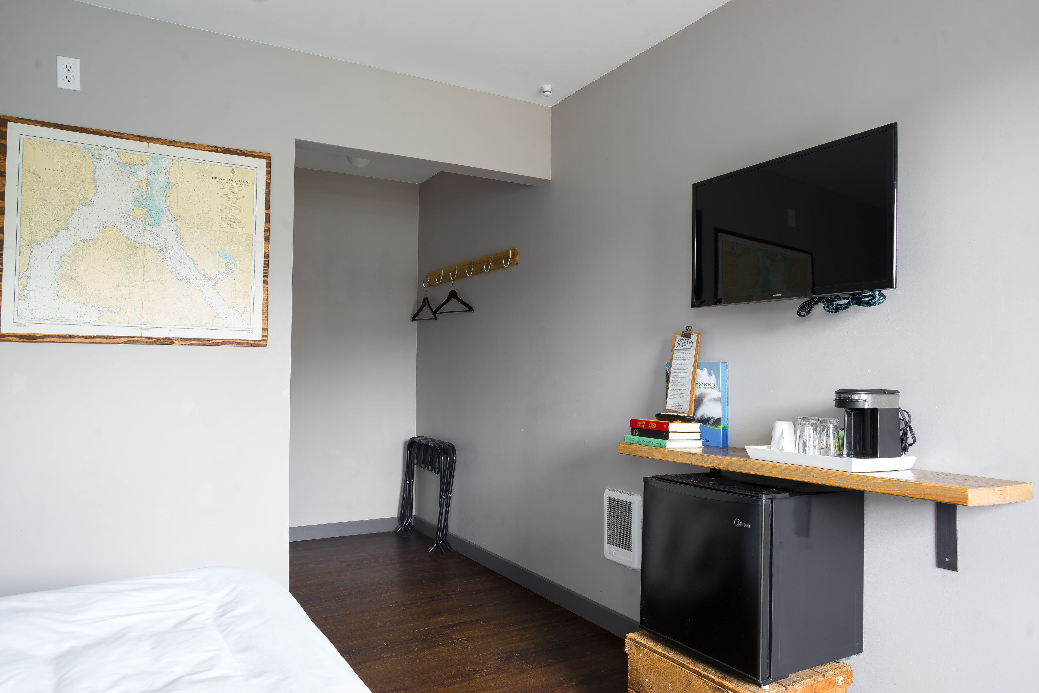 Een kleine hotelkamer met een bed, een kaart aan de muur, een televisie, een kleine koelkast, en een plank met boeken en een koffiezetapparaat.