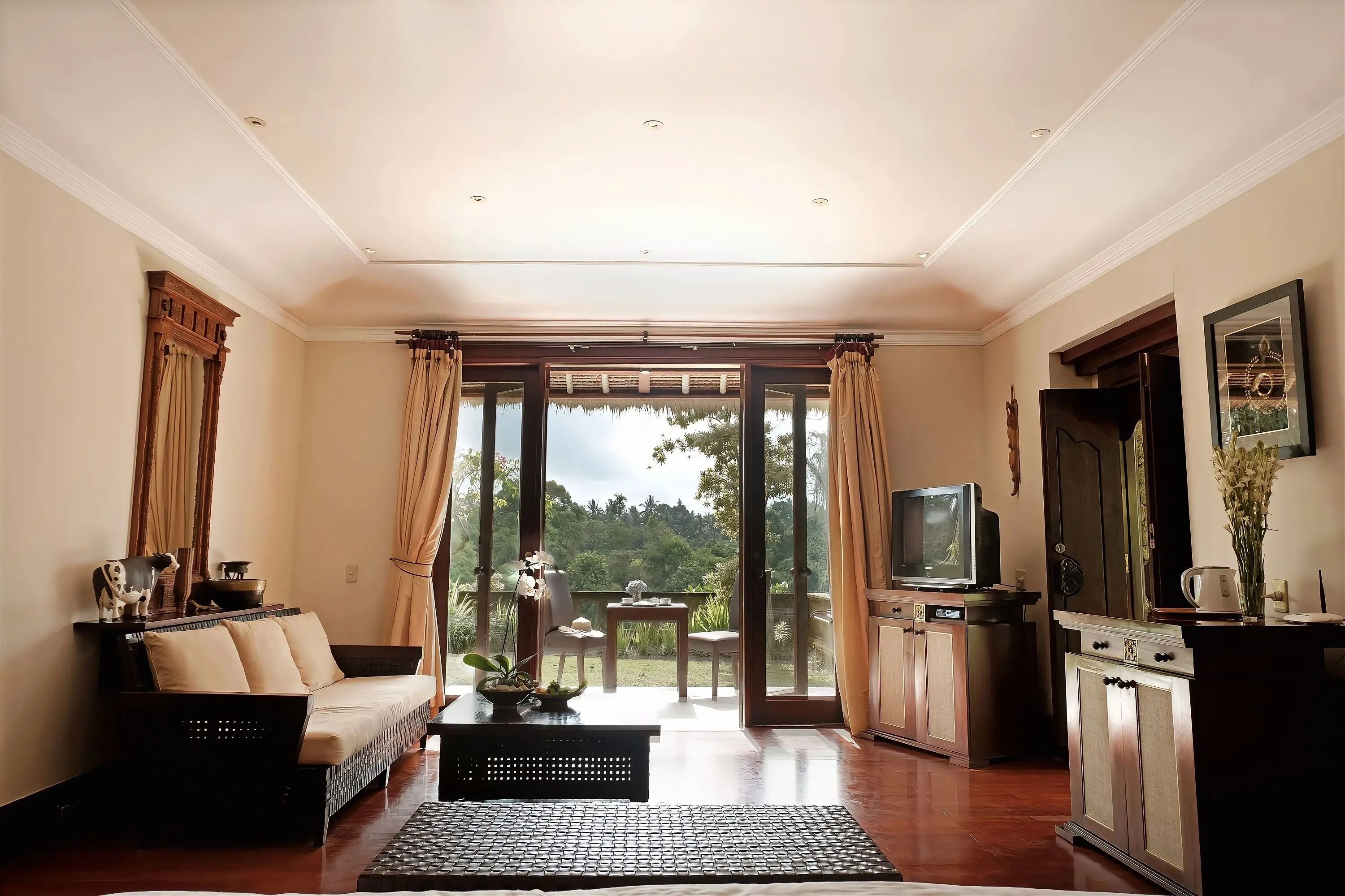 A spacious living room with a sofa, television, and a view of a lush garden through large sliding doors.