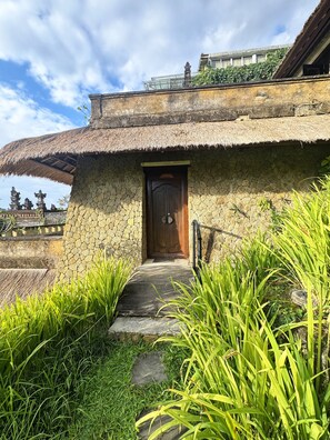 A traditional thatched-roof building with a wooden door, surrounded by lush greenery. - Anhera Suite Ubud (Ubud)
