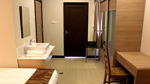 A hotel room with a bed, a bathroom with a sink and mirror, and a wooden desk. - Riverside Residence by Gina Suite (Bandar Seri Begawan)