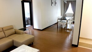 A living room with a beige sofa, a glass coffee table, and a dining area with a table and chairs. - Riverside Residence by Gina Suite (Bandar Seri Begawan)