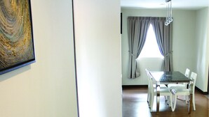 A dining area with a table and chairs, a window with curtains, and a painting on the wall. - Riverside Residence by Gina Suite (Bandar Seri Begawan)