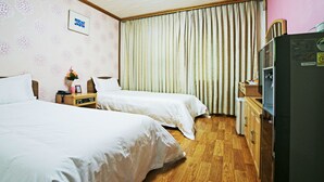 A hotel room with two beds, a wooden dresser, a refrigerator, and a window with curtains. - Emerald Hotel (Jeju City)