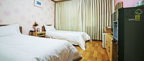 Habitación de hotel con dos camas, un aparador de madera, un refrigerador y una ventana con cortinas.