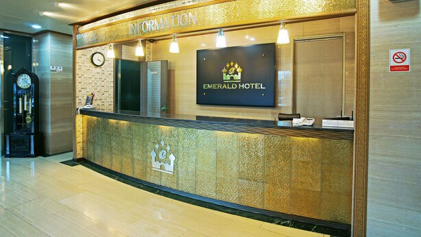 A reception desk at the Emerald Hotel with a clock, a sign for information, and a no-smoking sign. - Emerald Hotel (Jeju City)