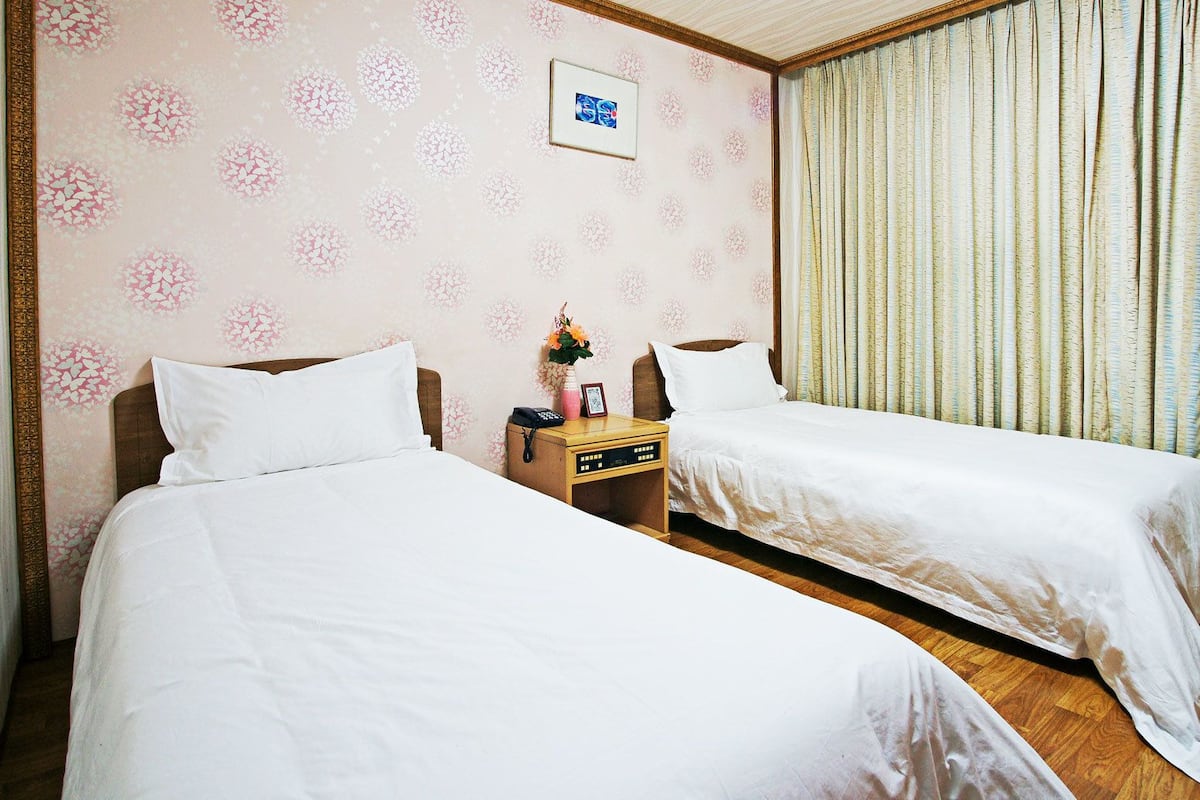 Camera d'albergo con due letti singoli, un comodino in legno, un tavolino e un quadro appeso al muro.