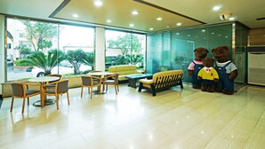 A hotel lobby with a seating area, a glass wall, and a view of the outside. - Emerald Hotel (Jeju City)