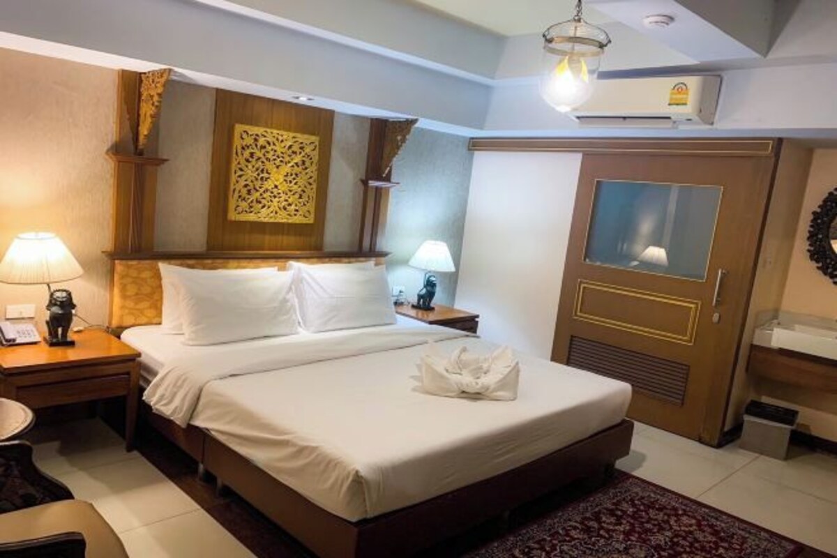 Habitación de hotel con una cama grande, cabecero de madera, dos mesitas de noche con lámparas, un armario y un panel decorativo en la pared.