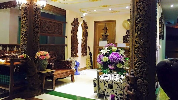 A traditional interior with ornate wooden carvings, a dining area with a table and chairs, and a decorative vase with flowers. - Kim Hostel at Morleng (Bangkok)