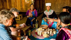 A group of people seated around a table with various food items and a bottle. - Lisu Lodge (Mae Taeng)