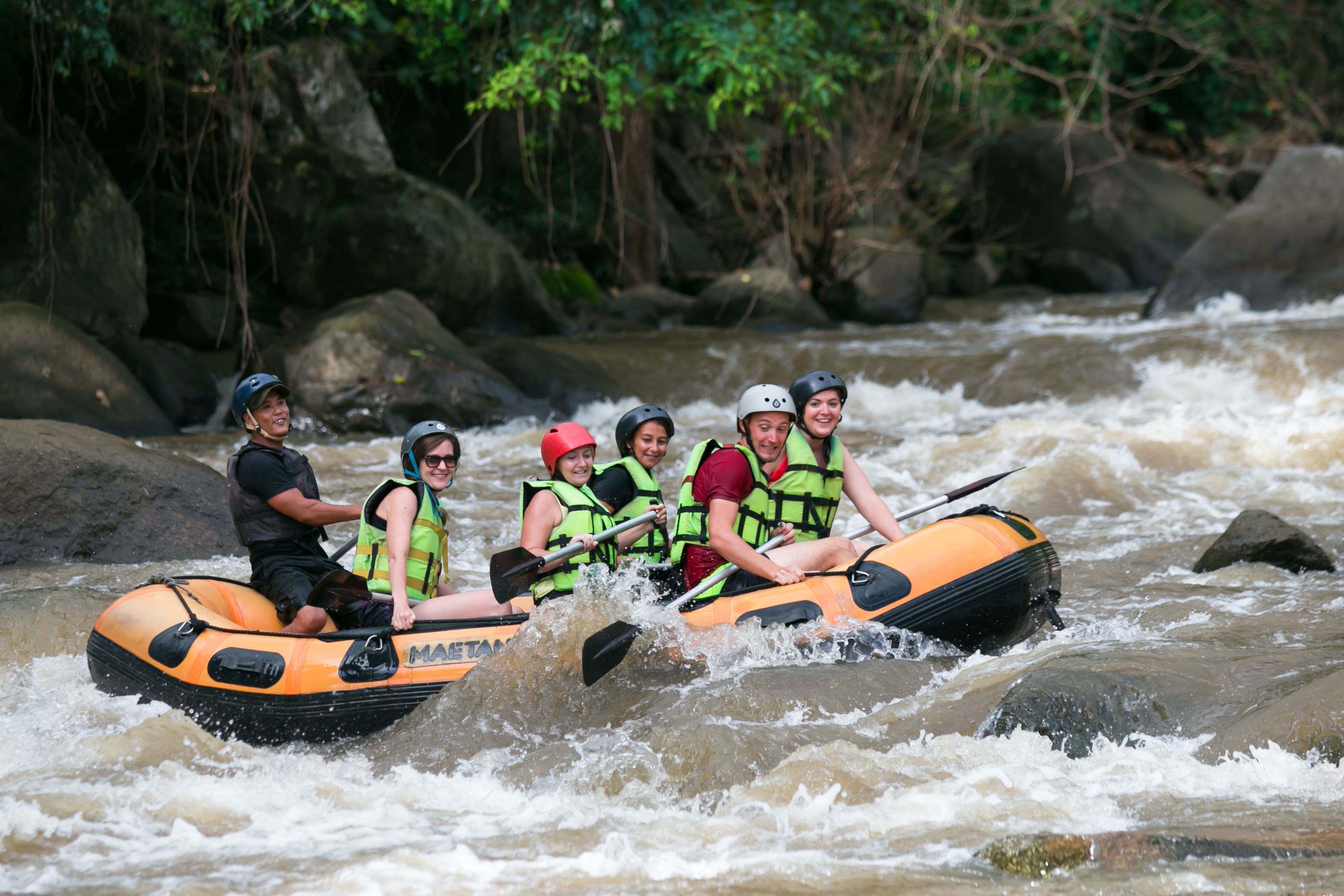 A group of people in an inflatable raft navigating a river surrounded by rocks and greenery.