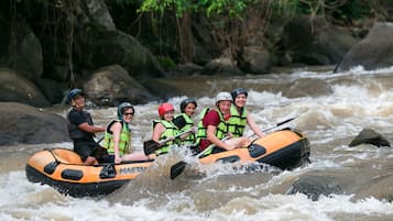 A group of people in an inflatable raft navigating a river surrounded by rocks and greenery.