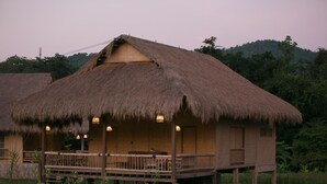 A thatched-roof bungalow with a wooden deck and a small porch, surrounded by lush greenery. - Lisu Lodge (Mae Taeng)