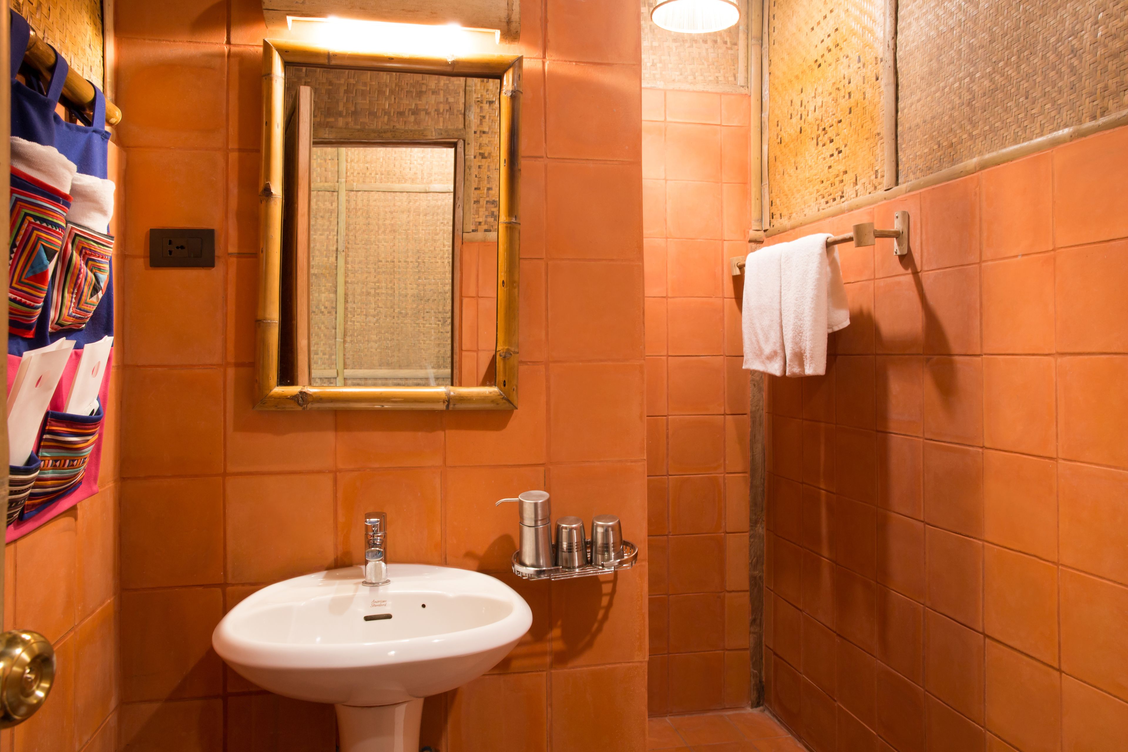 A bathroom with orange tiled walls, a white sink, a mirror, and a towel rack.