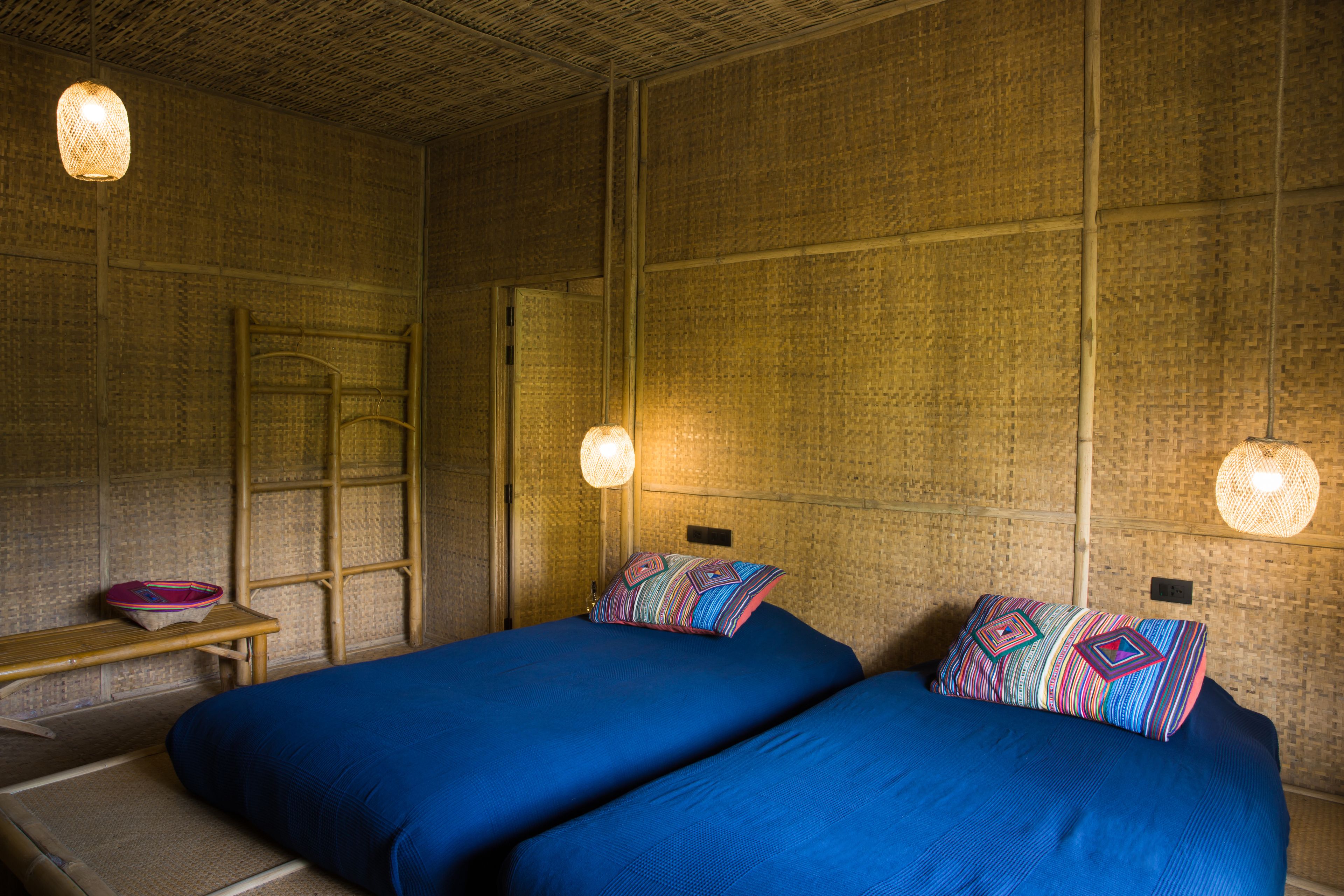 A room with two beds, a wooden bench, and a woven wall.