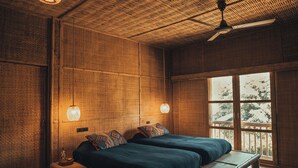 A room with a bed, a bench, a ceiling fan, and a window with a view of trees. - Lisu Lodge (Mae Taeng)