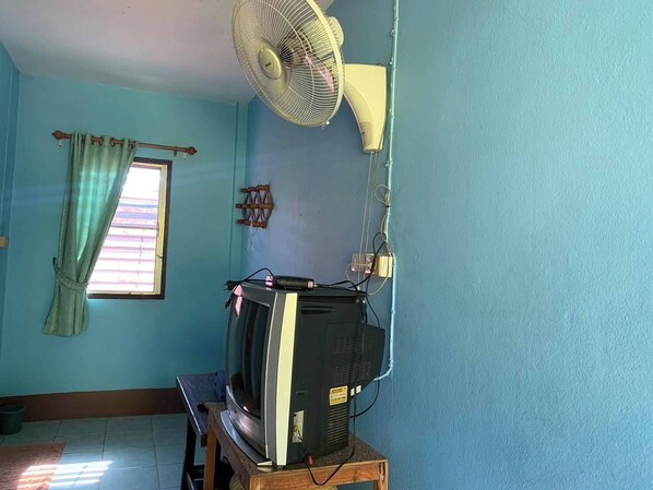 A room with a television on a wooden stand, a ceiling fan, a window with curtains, and a wall-mounted electrical outlet. - Ruenview Resort (Mae Chan)
