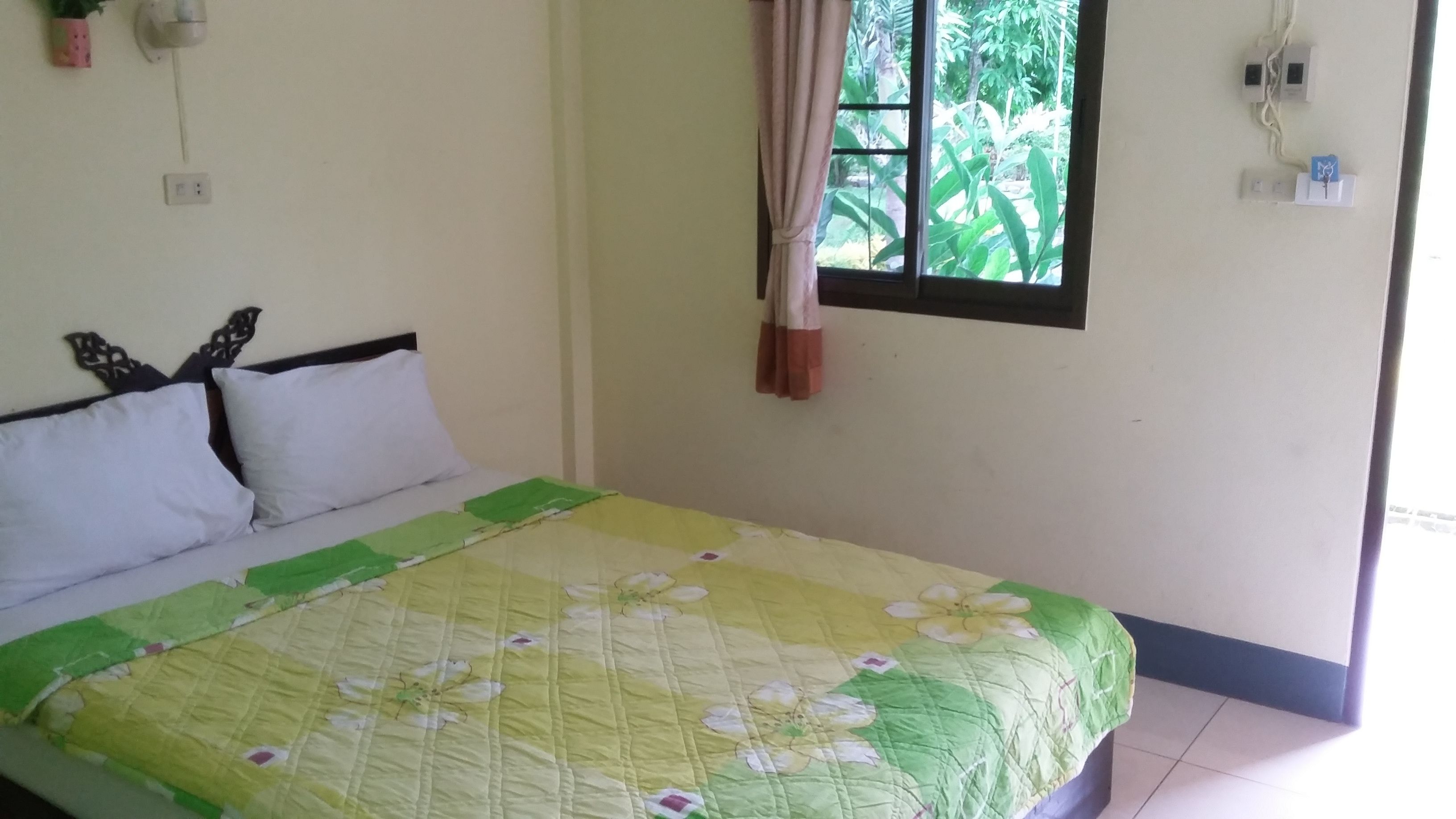 A bedroom with a bed, a window with curtains, and a wall-mounted power outlet.