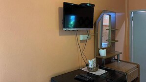 A room with a mounted TV, a wooden desk with a remote control, a mirror, and a small shelf with a tissue box. - Ruenview Resort (Mae Chan)
