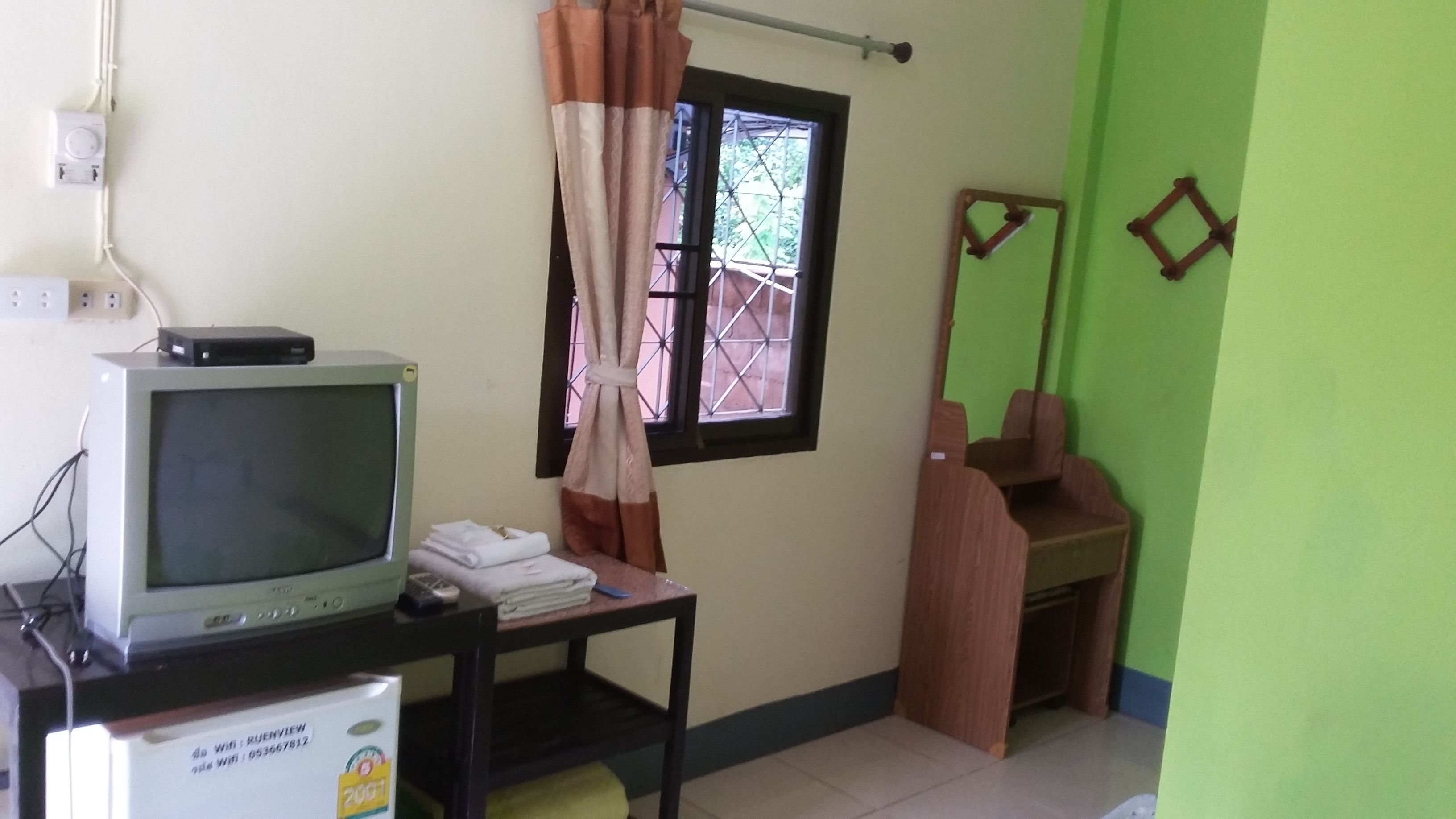 Una habitación con una televisión sobre una mesa, una ventana con cortina y una pared verde.