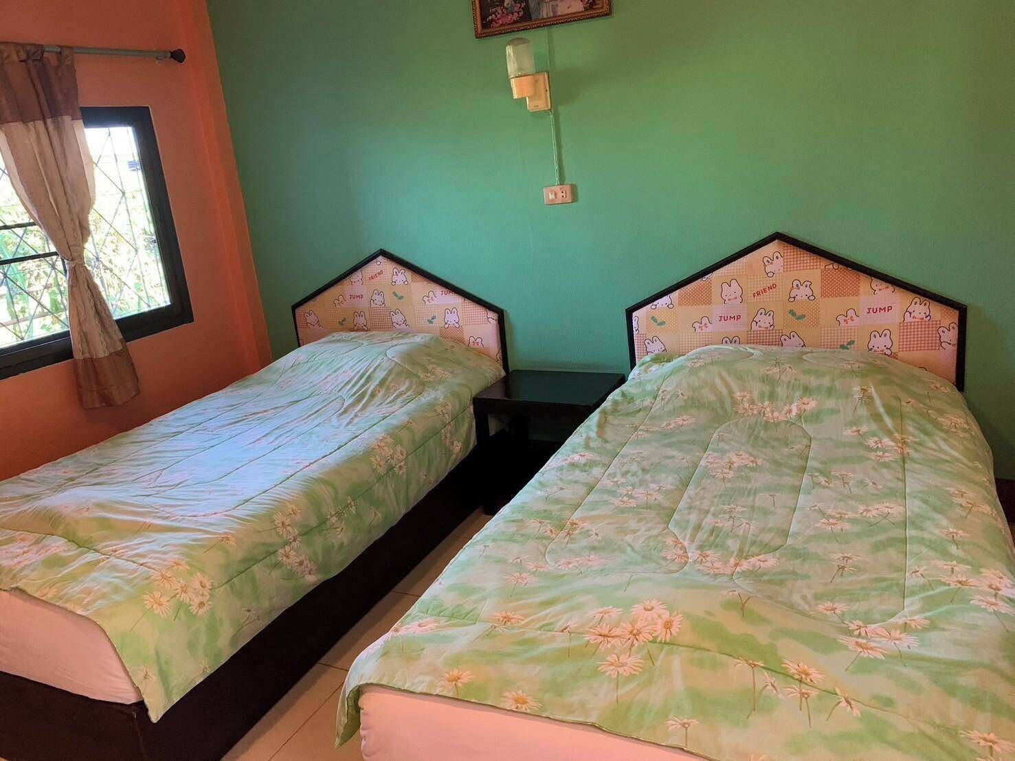 Dos camas individuales con ropa de cama estampada, una ventana con cortinas y una lámpara fijada a la pared.