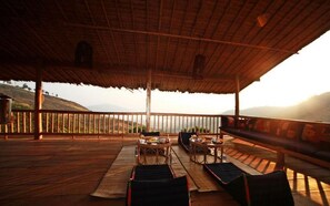 An outdoor wooden deck with seating and tables, overlooking a hilly landscape.