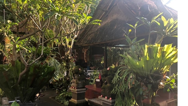 A traditional thatched-roof structure surrounded by lush greenery and potted plants. - Depa House (Ubud)