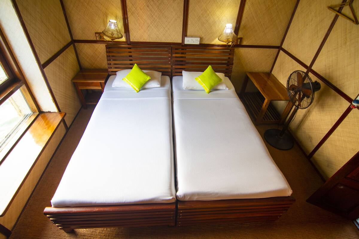 Una habitación con dos camas, cada una con una almohada, una mesita de noche, una lámpara y un ventilador.