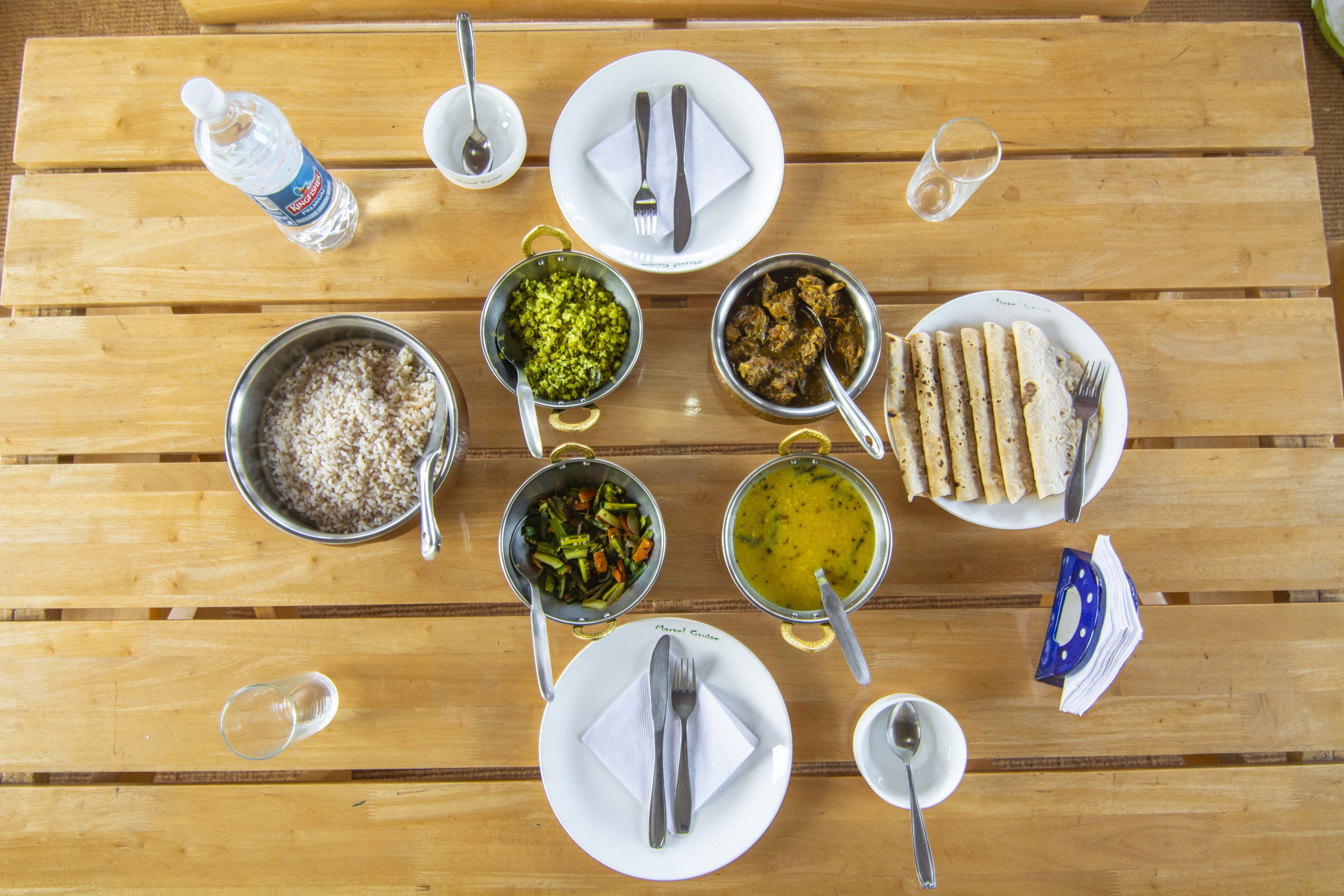 A wooden table with various dishes and utensils, including bowls of food, plates, and cutlery.