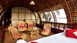 A room with wicker furniture, a bed, and a view of a body of water. - Marvel Cruise (Kuttanad Taluk)
