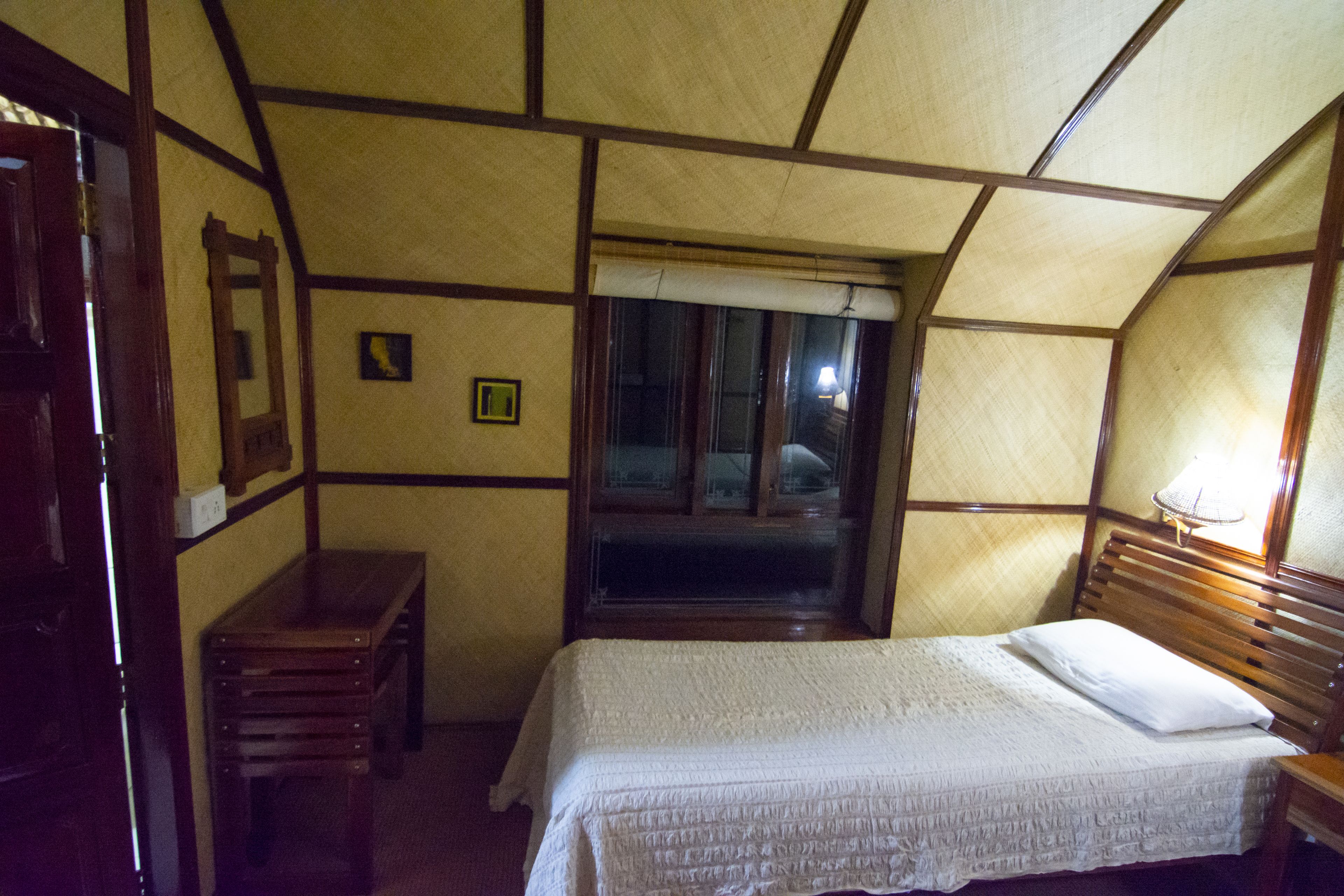 Ein Zimmer mit einem Bett, einem Nachttisch aus Holz, einem Fenster und einem kleinen Tisch.