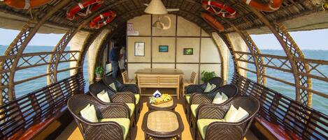 A boat interior with wicker furniture, a central table, and life preservers hanging from the ceiling.