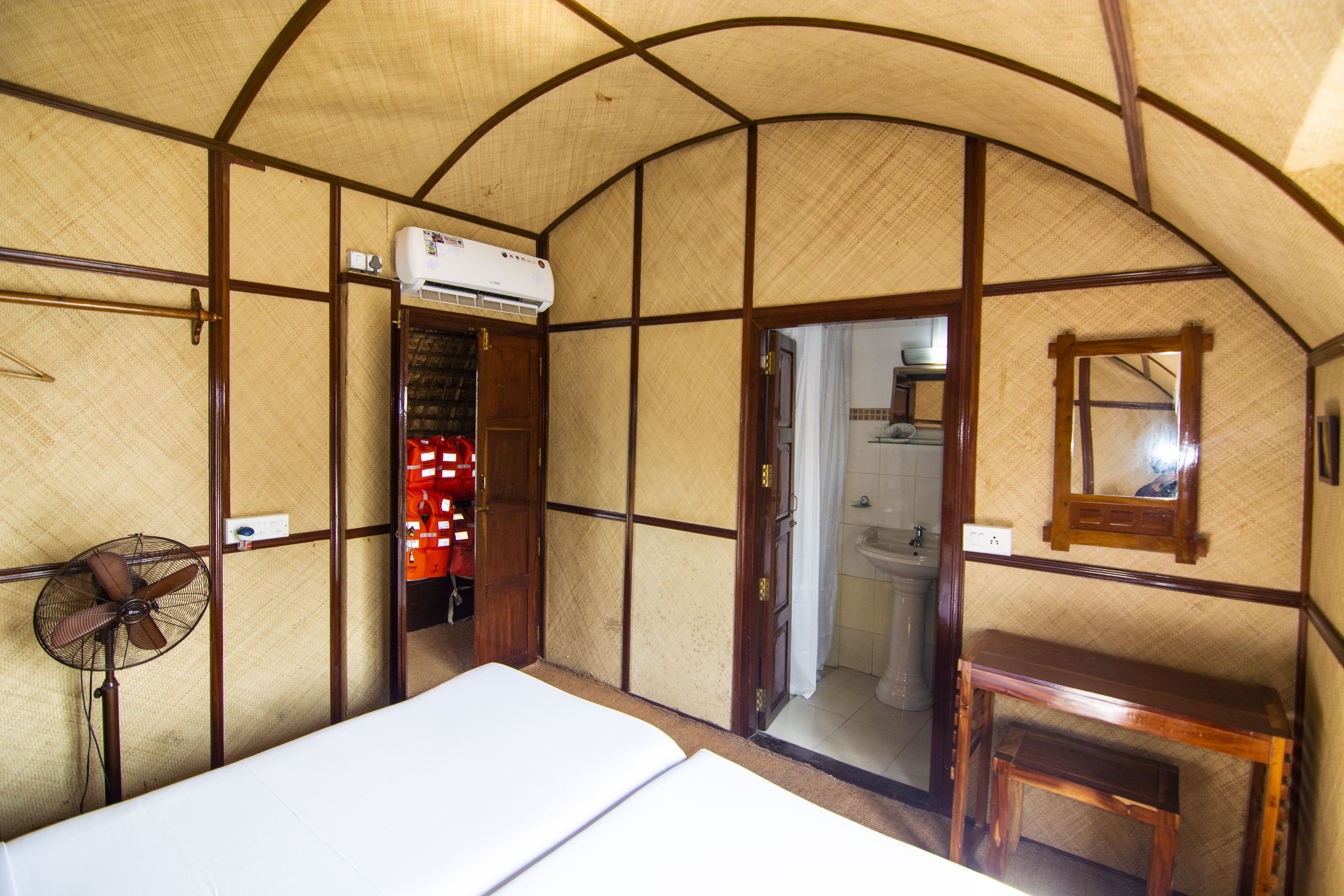 Una habitación con cama, ventilador, mesa de madera y aire acondicionado.