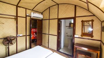 Una habitación con cama, ventilador, mesa de madera y aire acondicionado.