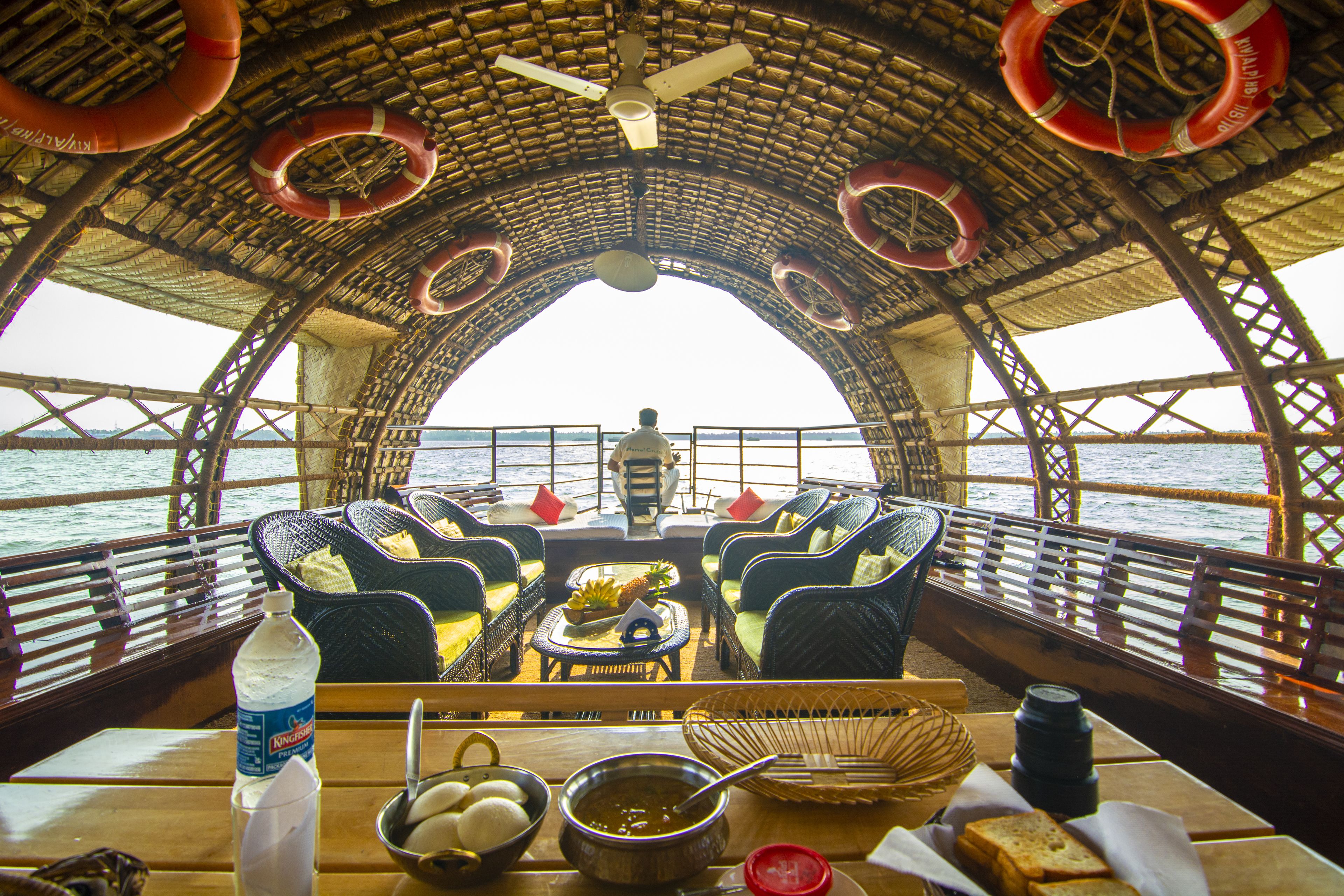 A boat with a thatched roof, wicker furniture, and a table set for dining.