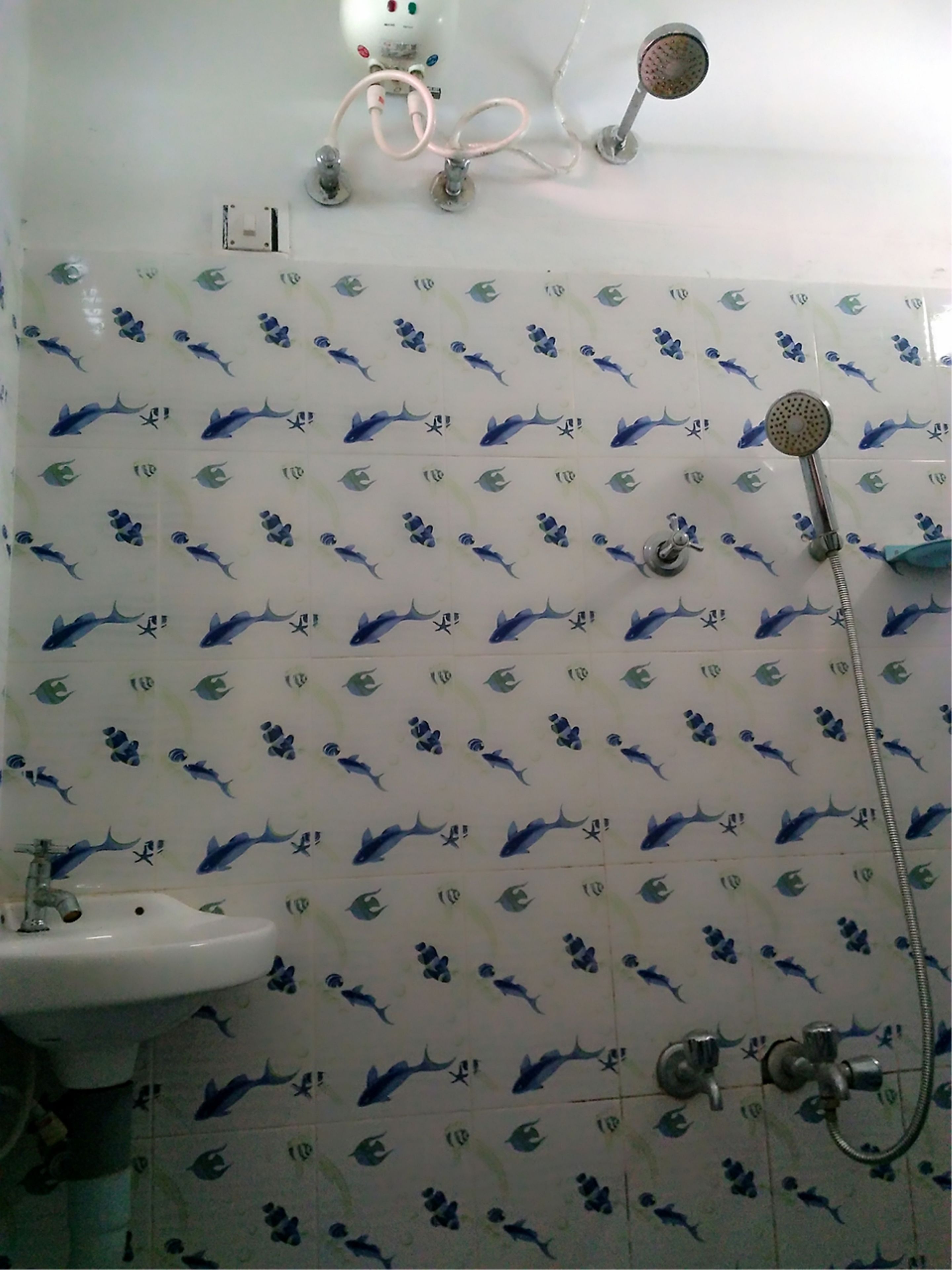 A bathroom with shark-themed tiles, a sink, and a shower with a hose.
